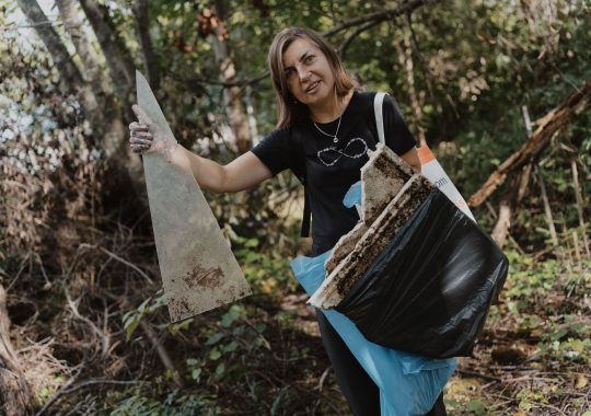 Savanorė miške laiko surinktas atliekas ir šiukšlių maišą